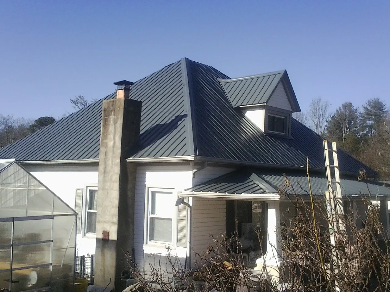 Dark blue standing seam metal roof on a white farmhouse with dormer — Slate & Tile Roof Repair by Roofing Brothers in Friendsville