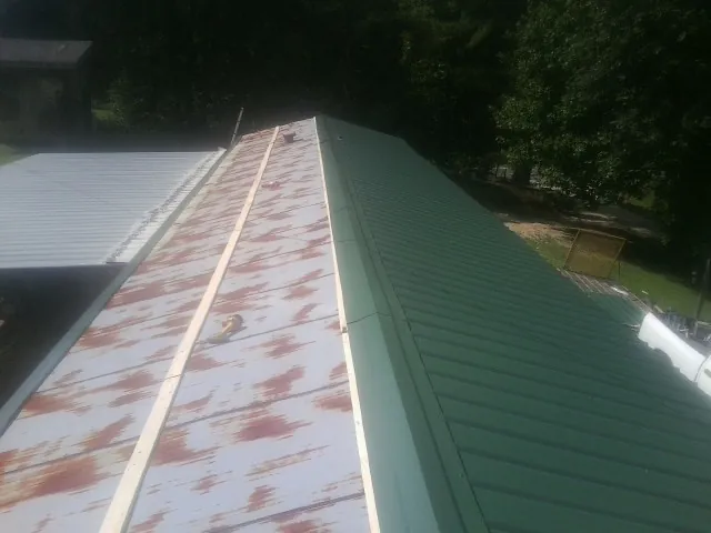 Old rusted panels beside newly installed green metal roofing — Wind Damage Roof Repair by Roofing Brothers in Friendsville