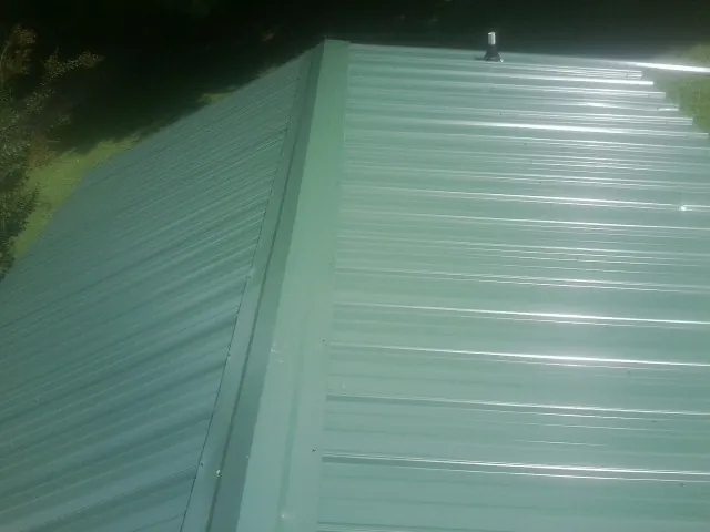 New green metal panels meeting at the ridge of a roof — Flat Roof Repair work by our crew in Friendsville