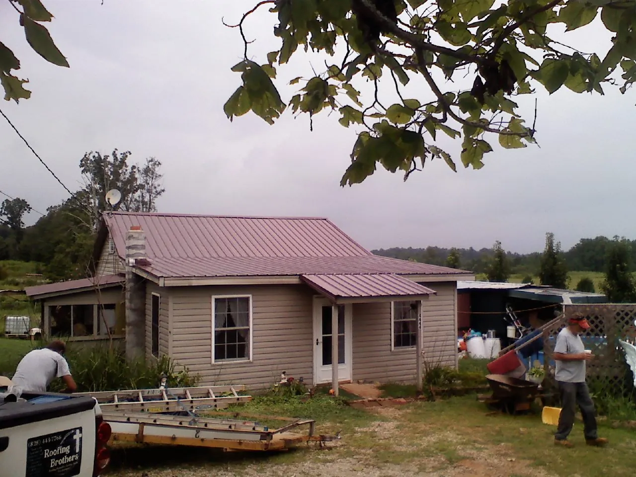Crew finishing a mauve metal roof on a small farmhouse in Friendsville